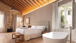 Un dormitorio con una cama grande, una mesita de noche de madera, una bañera blanca y vistas a zonas verdes.