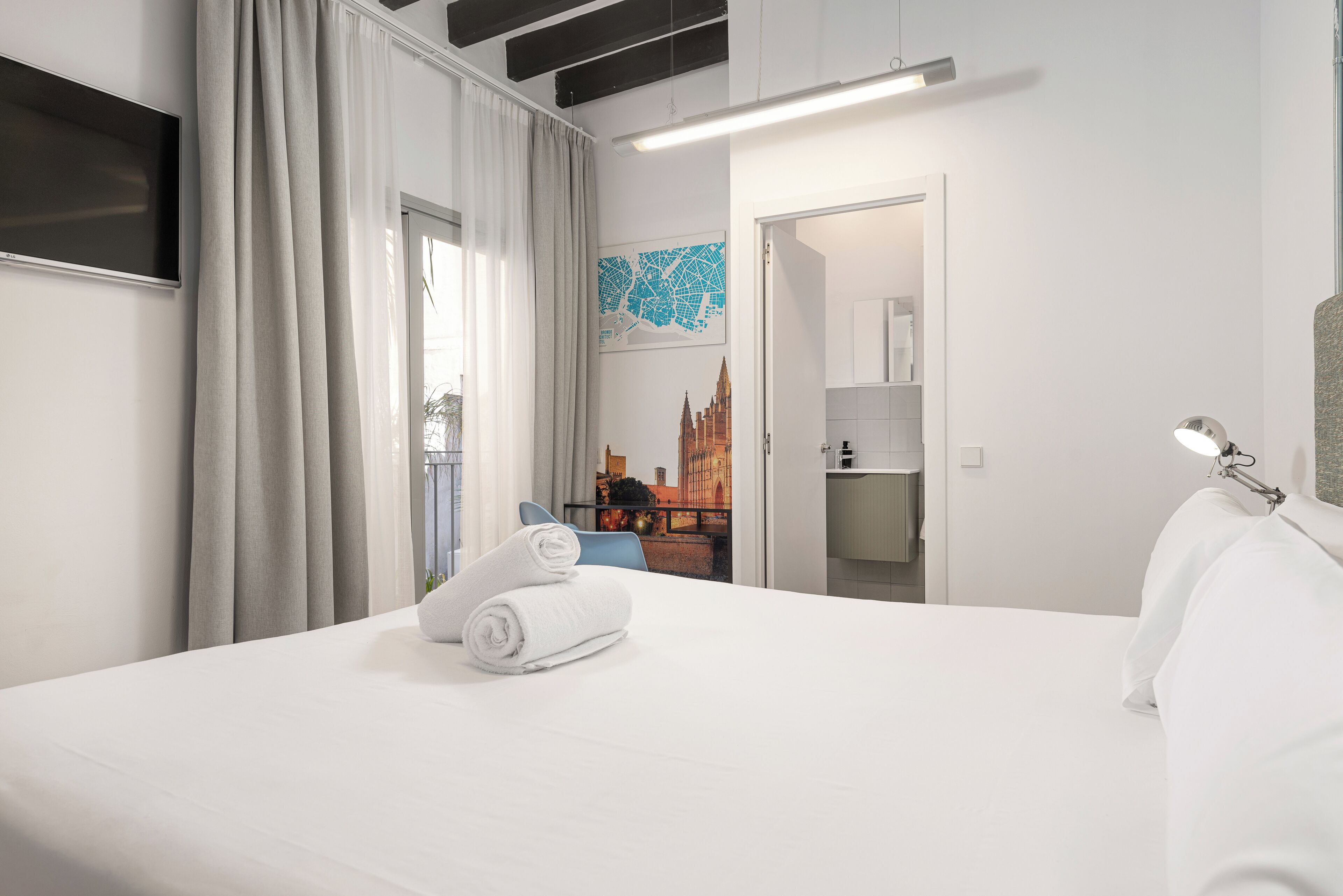 Habitación de hotel con cama, televisión de pantalla plana, un mapa en la pared y baño visible a través de una puerta abierta.
