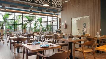 Un restaurante con mesas y sillas de madera, amplias ventanas que ofrecen vistas a zonas verdes y un diseño de techo moderno.