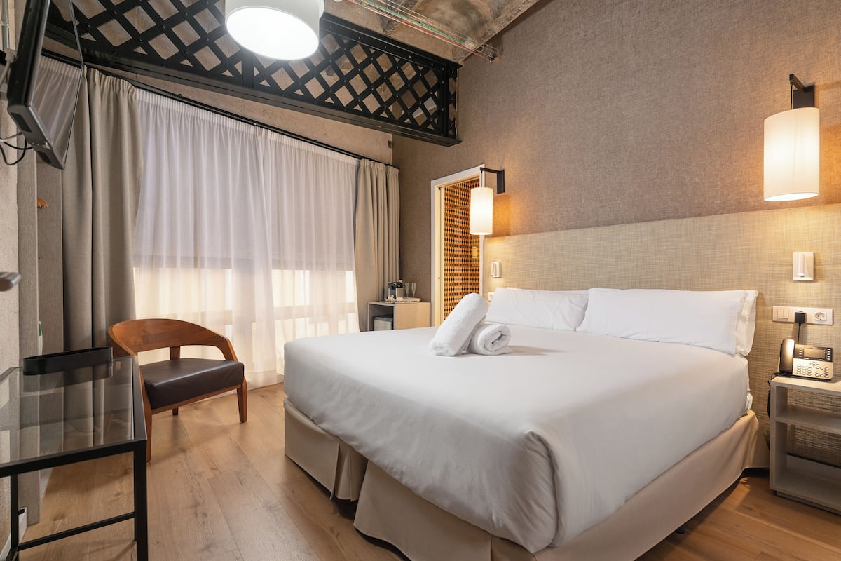 Una habitación de hotel con una cama grande, una silla de madera, un escritorio y un teléfono.