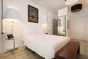 Habitación de hotel con una cama grande, lámparas de noche, teléfono en la mesita, un espejo y un cartel en la pared.