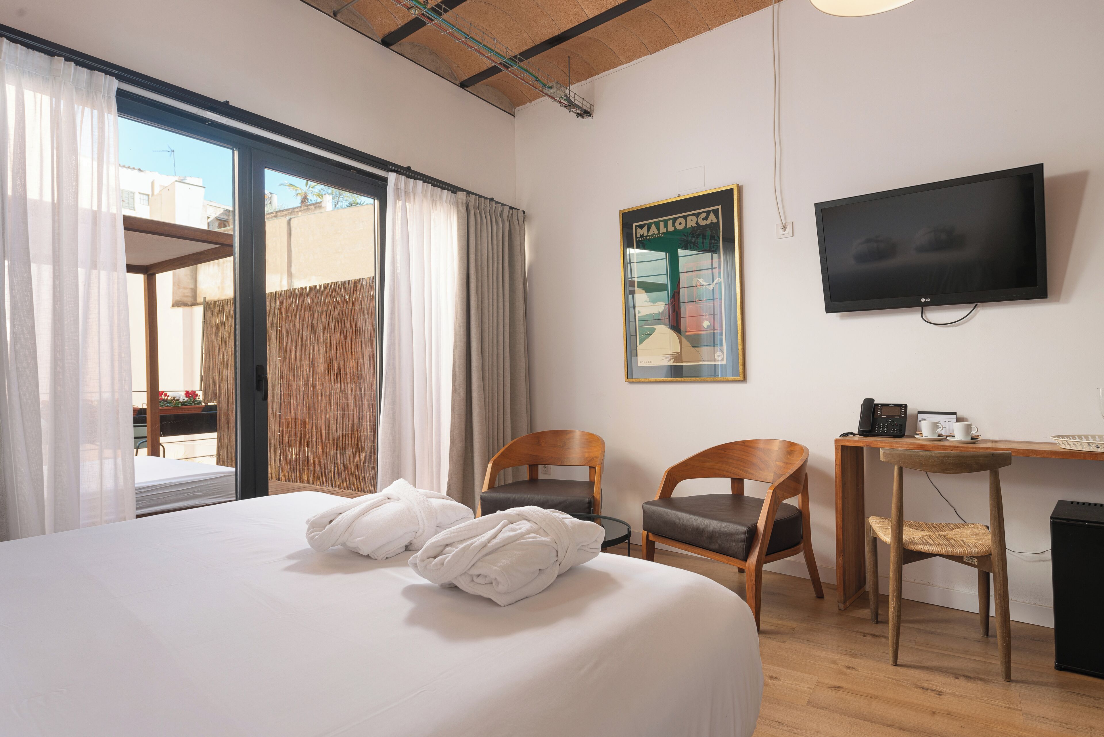 A hotel room with a bed, two chairs, a desk, a television, and a large window with curtains.