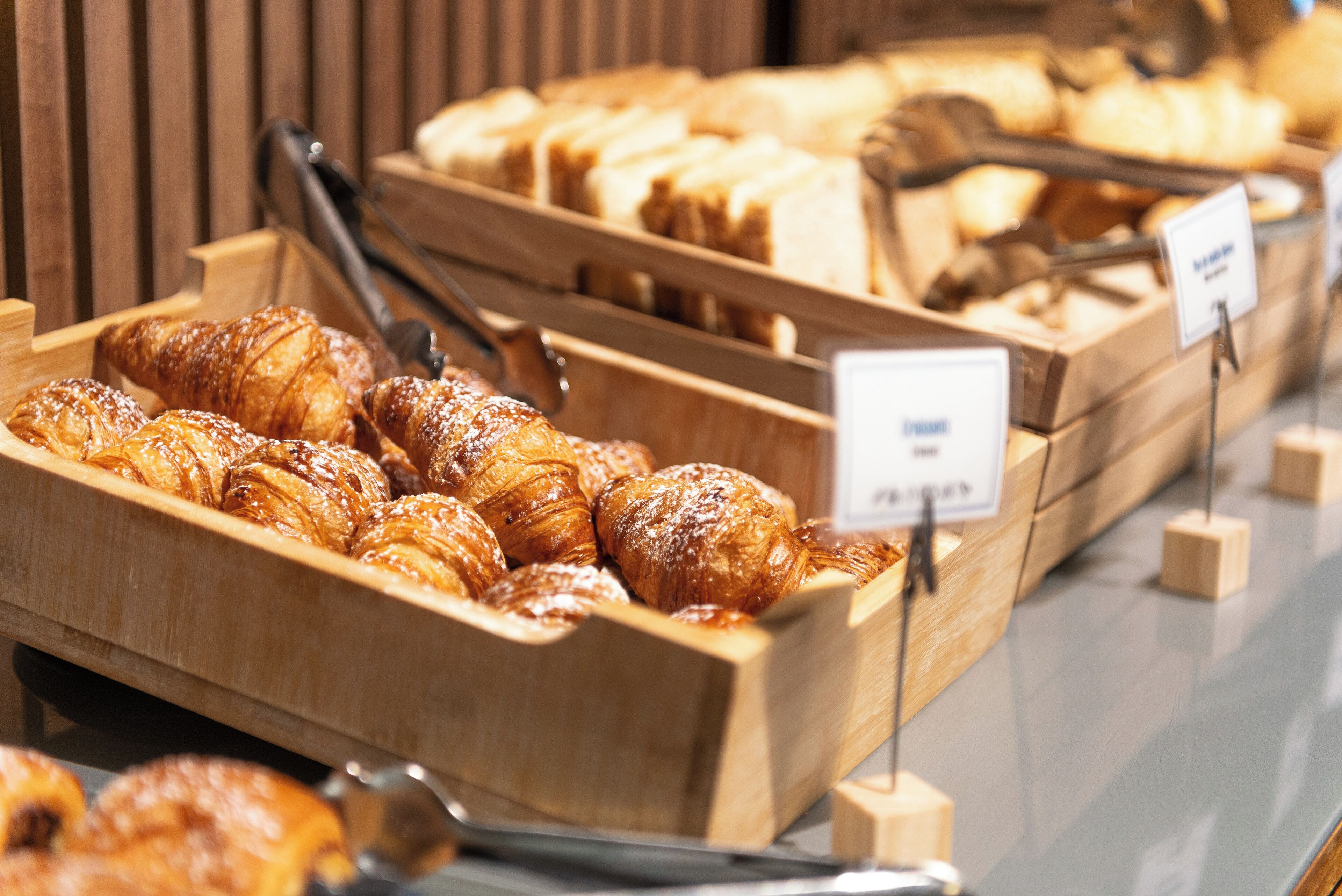 A bakery display with various baked goods, including croissants and bread, arranged in wooden trays.