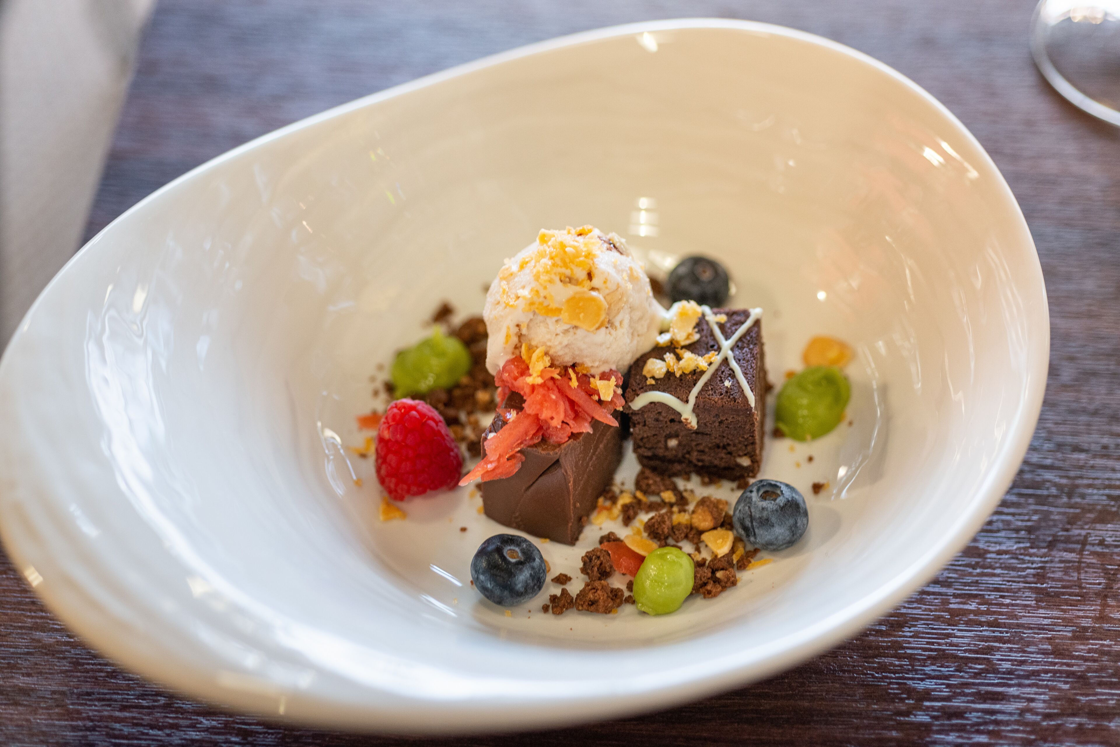A dessert in a white bowl with various fruits and chocolate pieces.