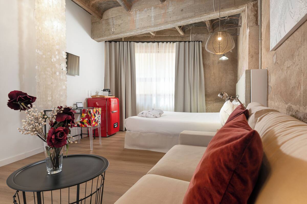Una habitación de hotel moderna con cama, sofá y una mesita con un jarrón de flores.