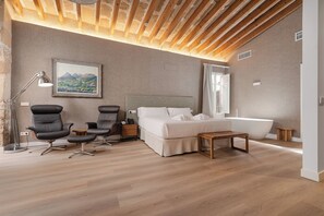 A bedroom with a large bed, two chairs, a nightstand, a desk, a lamp, a painting, a bathtub, and a wooden ceiling. - Brondo Architect Hotel (Palma de Mallorca)