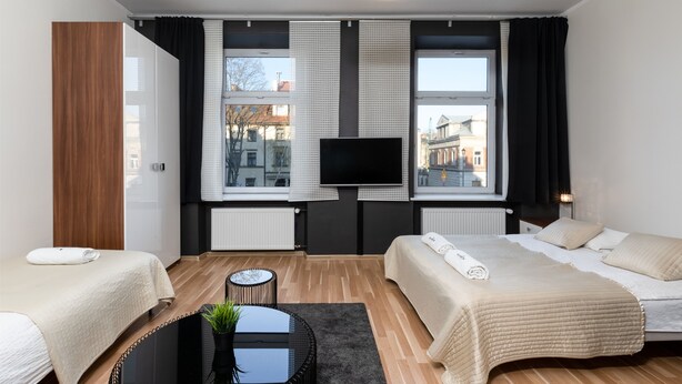 Una habitación de hotel moderna con dos camas, un televisor de pantalla plana, ventanas amplias y vista a la ciudad.