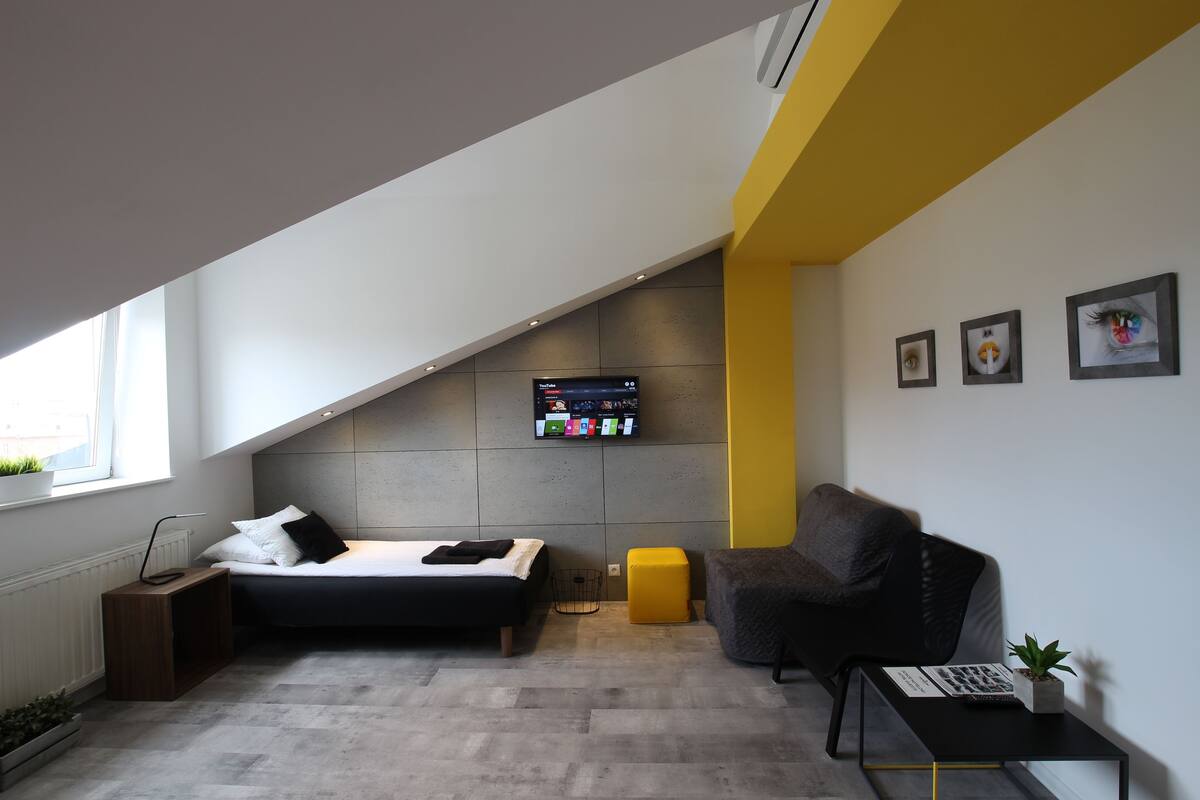 Un dormitorio moderno con cama, escritorio, silla y televisor montado en la pared.