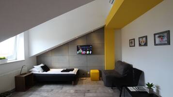 A modern bedroom with a bed, a desk, a chair, and a TV mounted on the wall.
