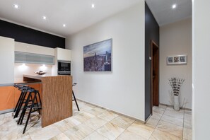 A modern kitchen with a bar area, a cityscape painting, and a vase with decorative sticks. - Rainbow Apartments 1 (Kraków)