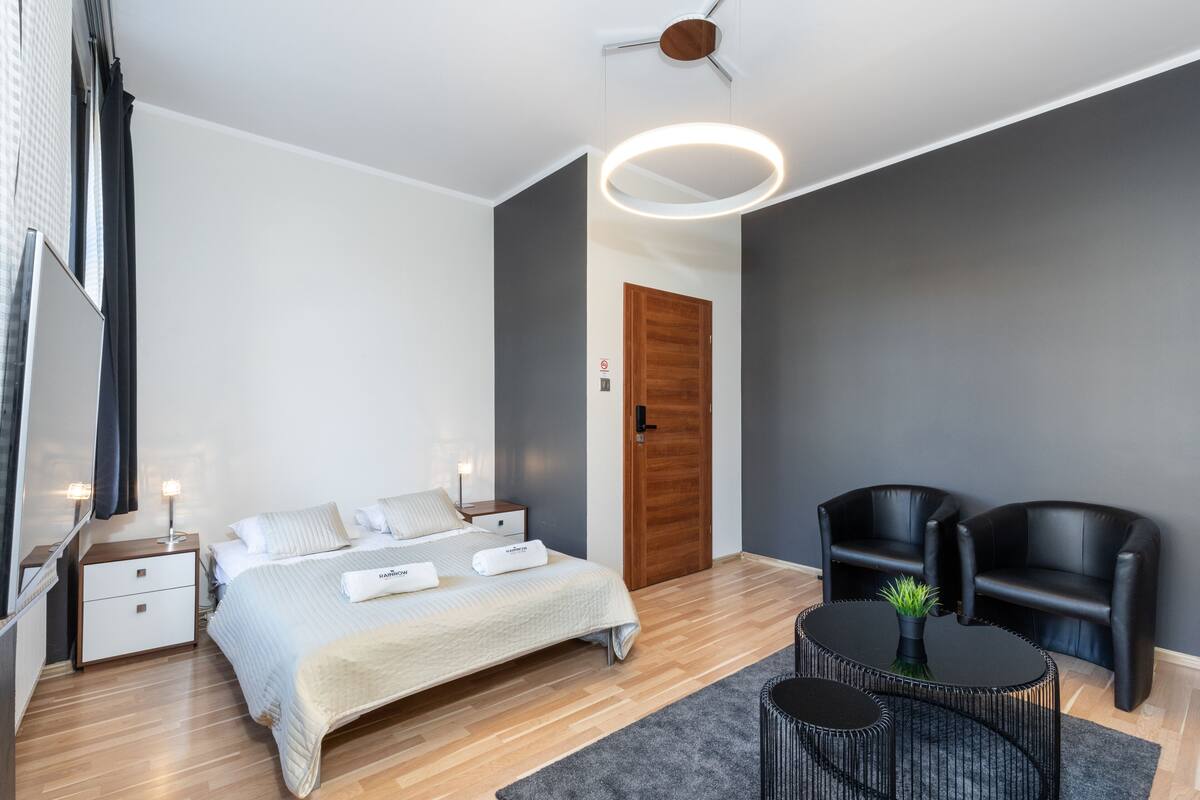 Un dormitorio moderno con cama, mesitas de noche, una mesa redonda y dos sillas negras.