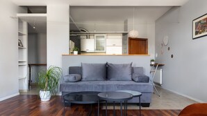 Una sala de estar moderna con un sofá gris, dos mesitas auxiliares negras, una planta en maceta y suelo de madera.