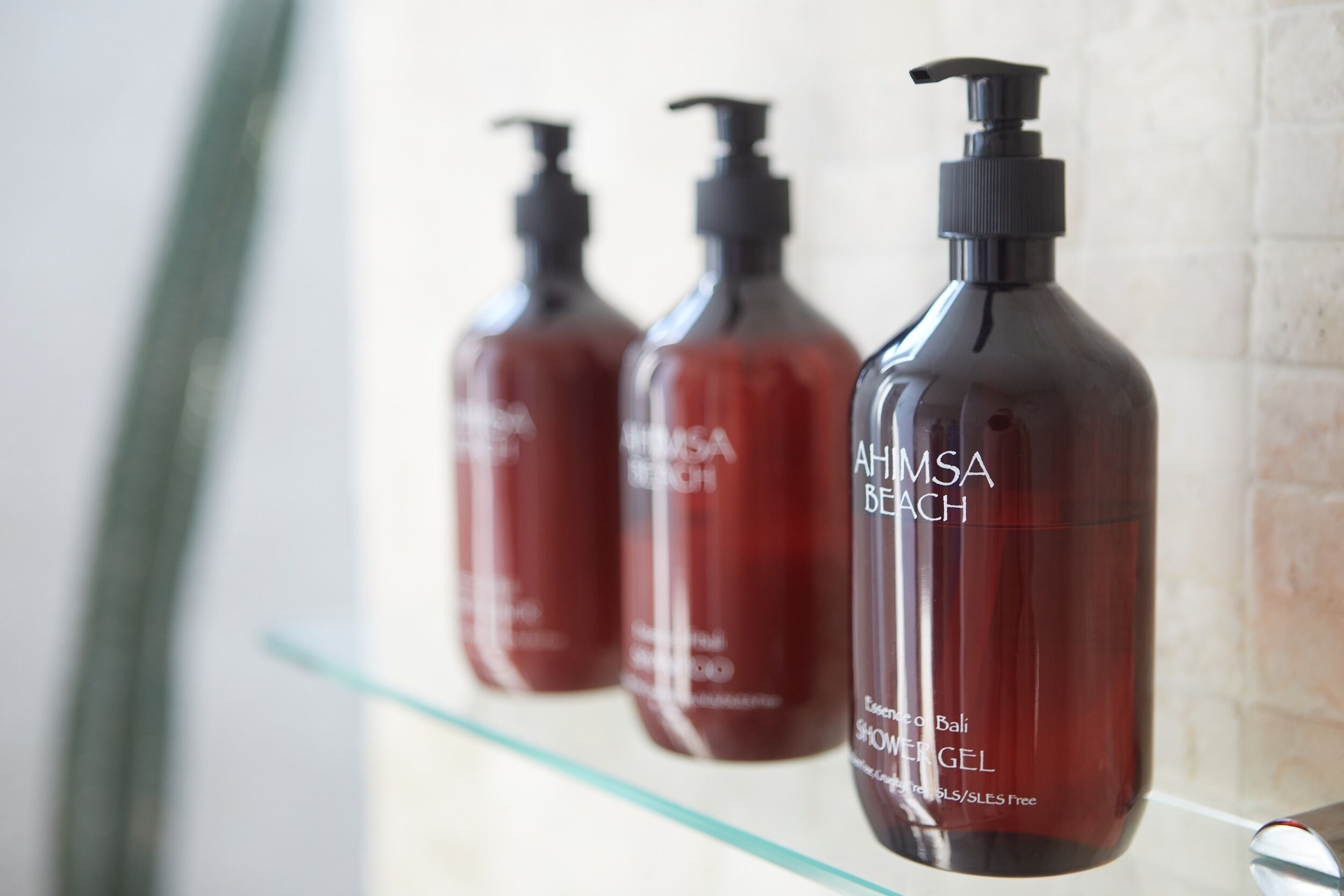 Three bottles of AHMASA BEACH shower gel on a glass shelf.