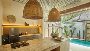 Cocina moderna con encimera de mármol, estufa a gas y una isla grande con taburetes de bar. Se ve una piscina a través de las puertas de cristal.