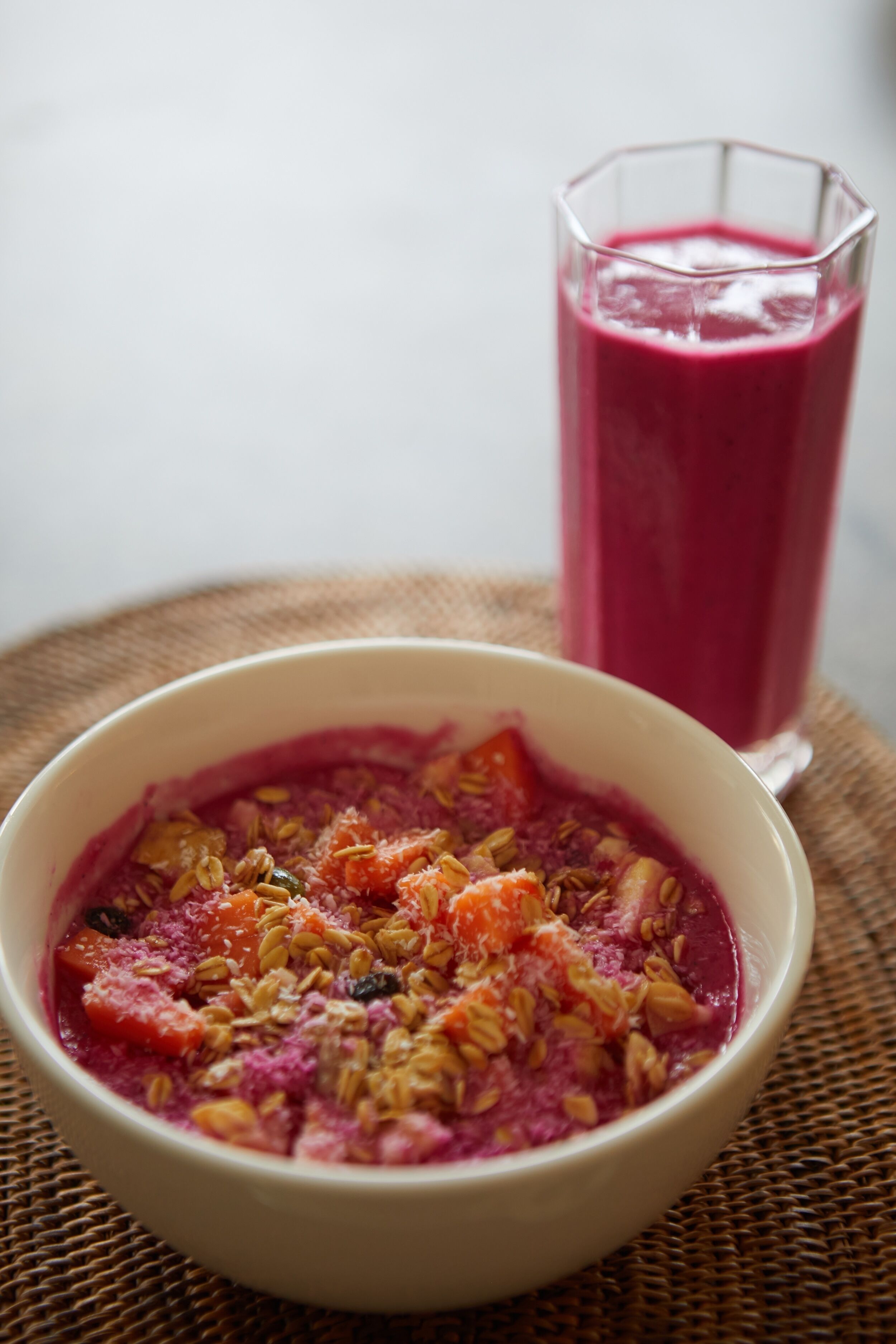 A bowl of food with a glass of pink smoothie in the background.