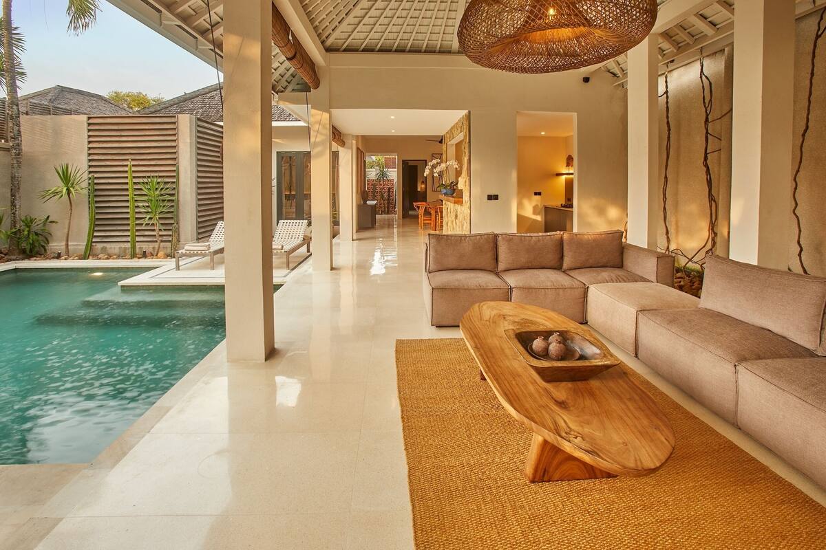 Un espacio moderno con piscina, una mesa de centro de madera y un sofá color beige.