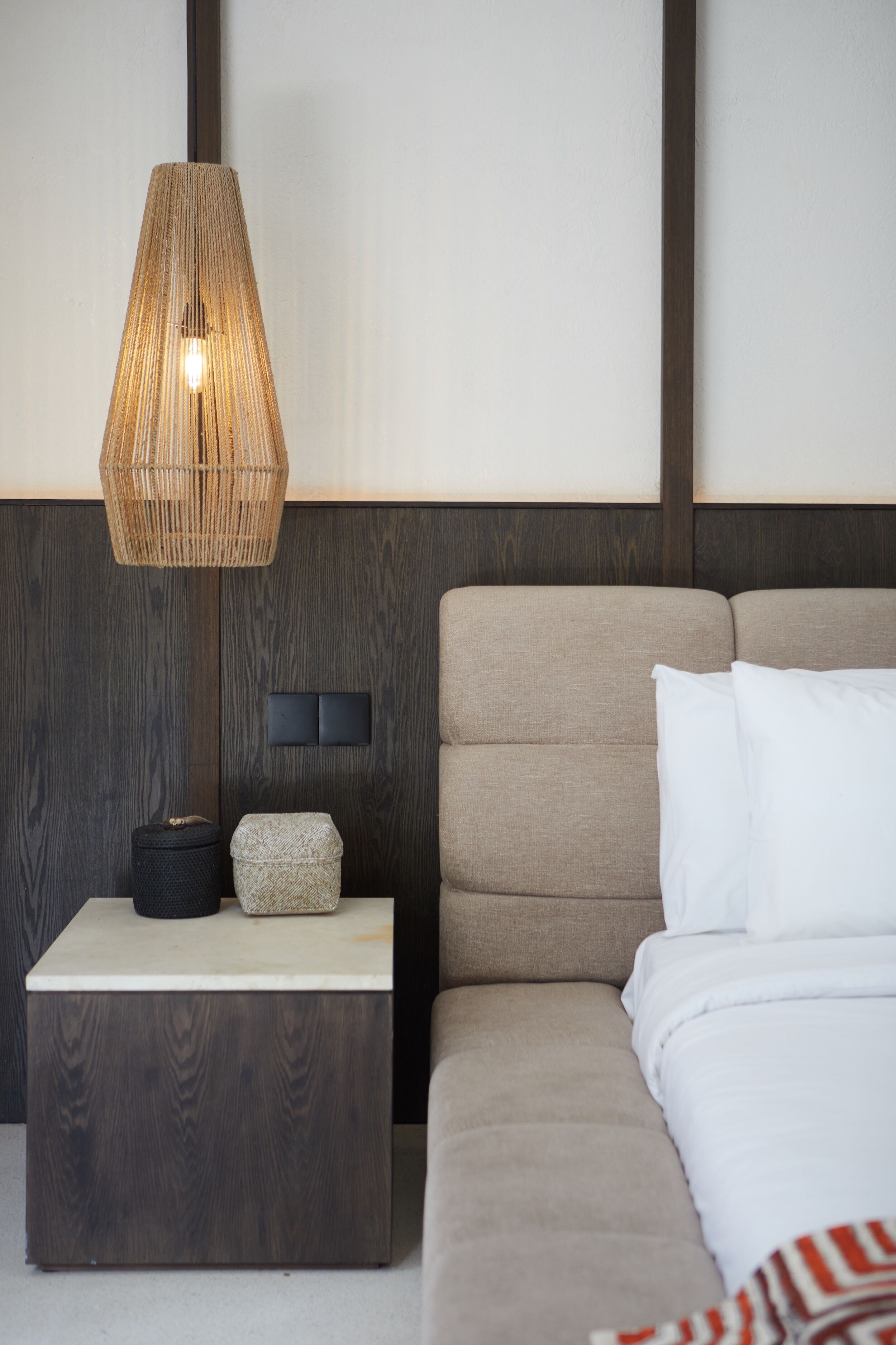 A modern bedroom with a wooden headboard, a bedside table with a lamp, and a bed with white bedding.