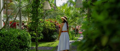 A woman in a white dress standing on a pathway surrounded by lush greenery and tropical plants.
