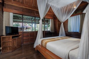 Una habitación de madera con una cama, un televisor sobre un mueble de madera y ventanas con cortinas.