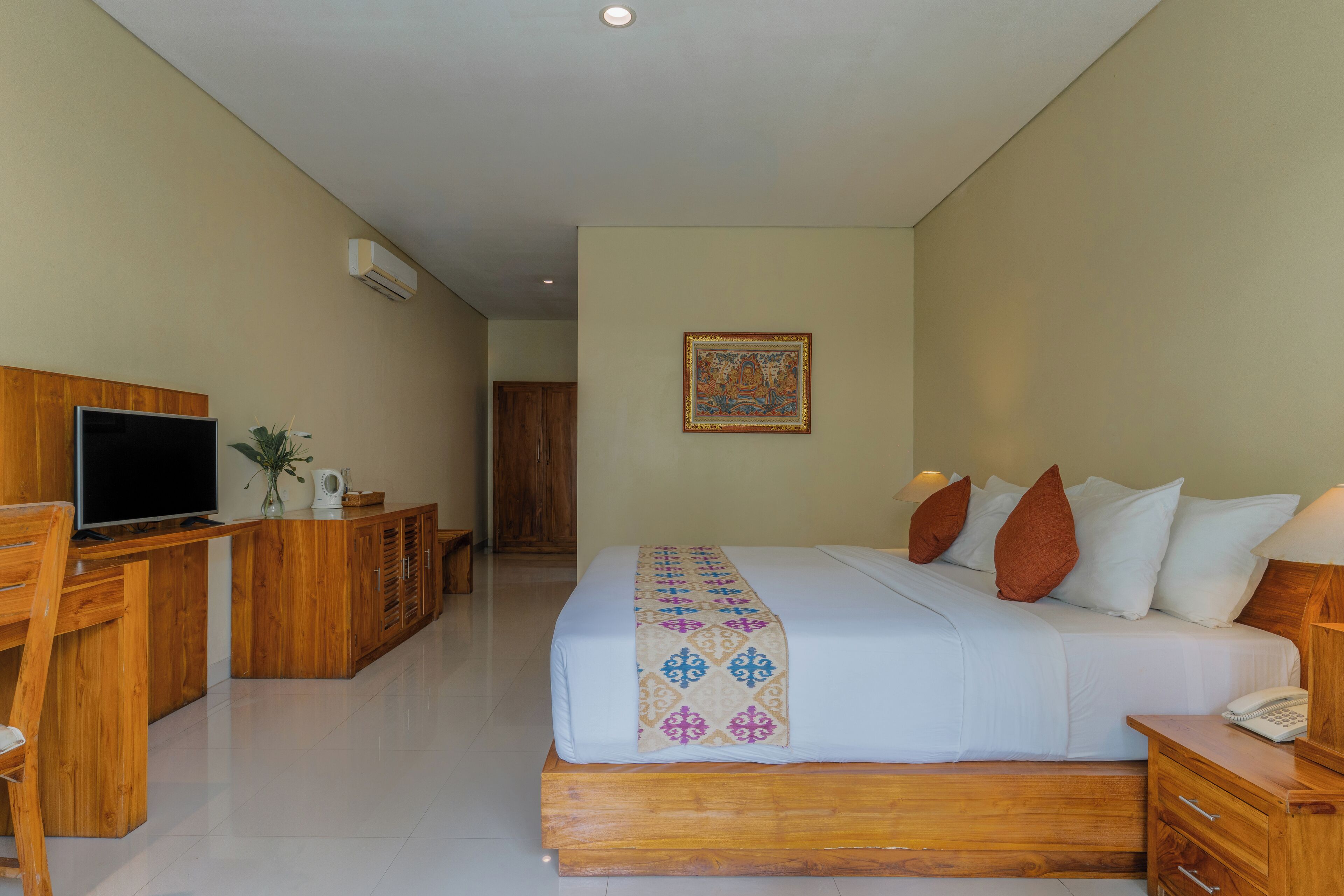 A hotel room with a bed, a wooden desk with a television, a telephone, and a decorative pillow.
