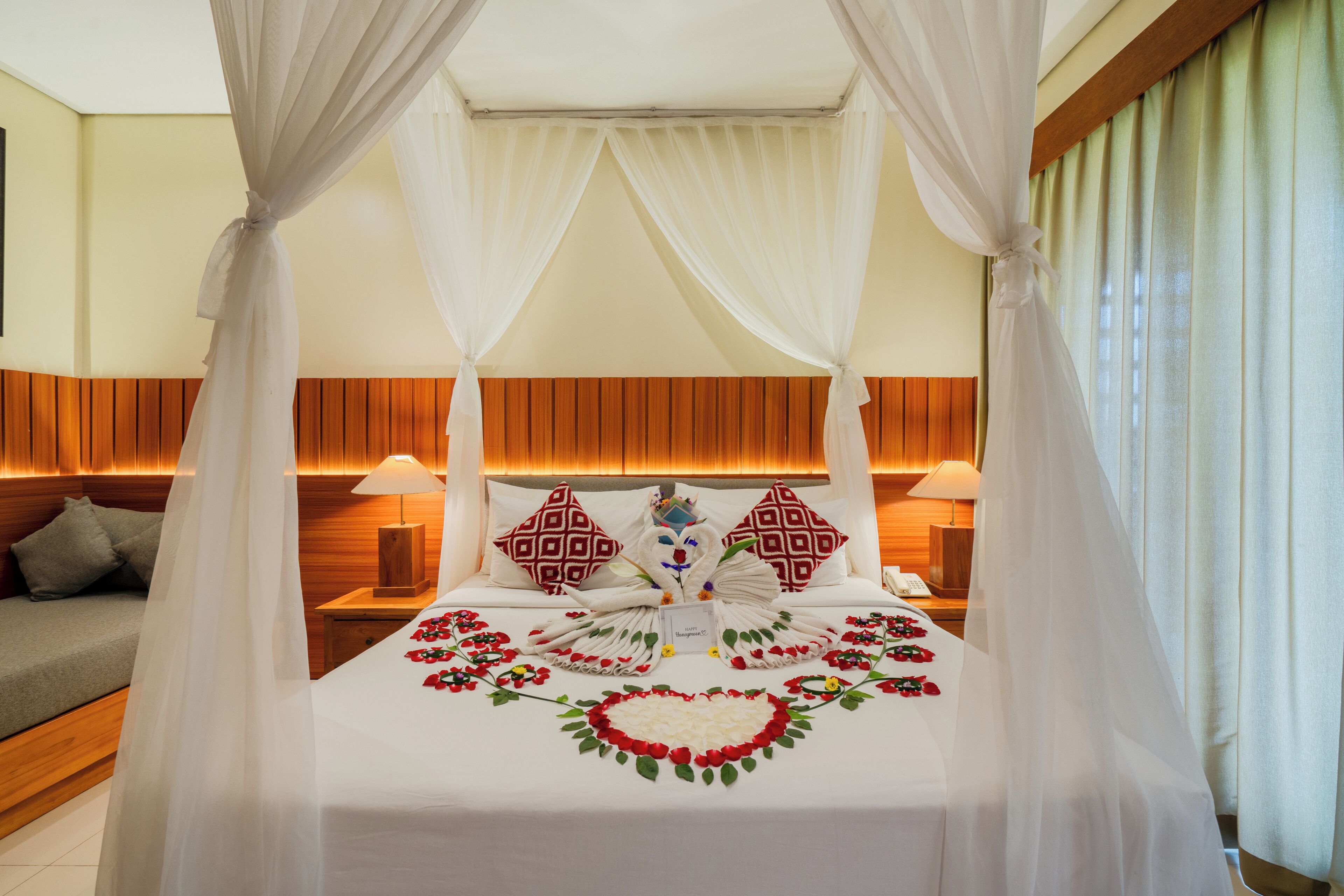 A bed with a canopy, a bedside table with a lamp, and a decorative floral arrangement on the bed.