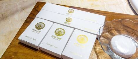 Una bandeja de madera con cuatro cajas blancas etiquetadas 'pertiwi' y 'shower cap', y un recipiente de vidrio transparente con una sustancia blanca.