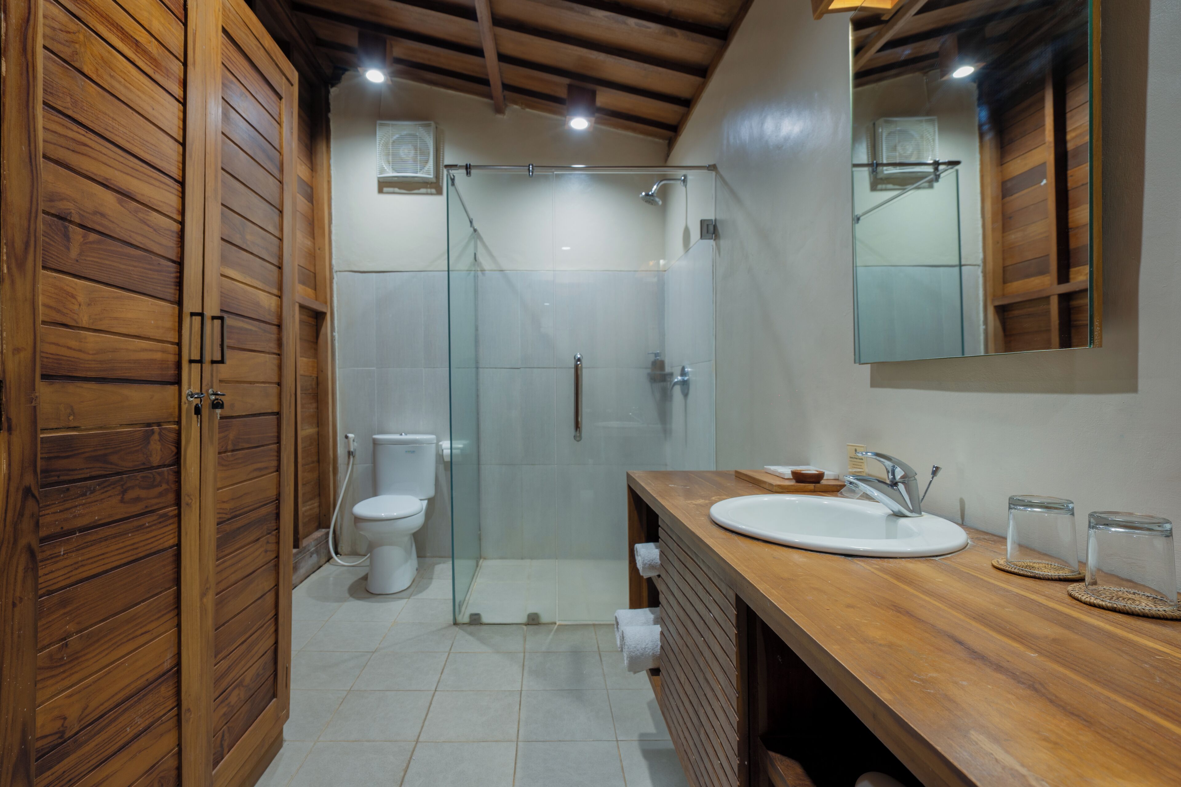 A modern bathroom with a wooden vanity, a glass shower enclosure, and a large mirror.