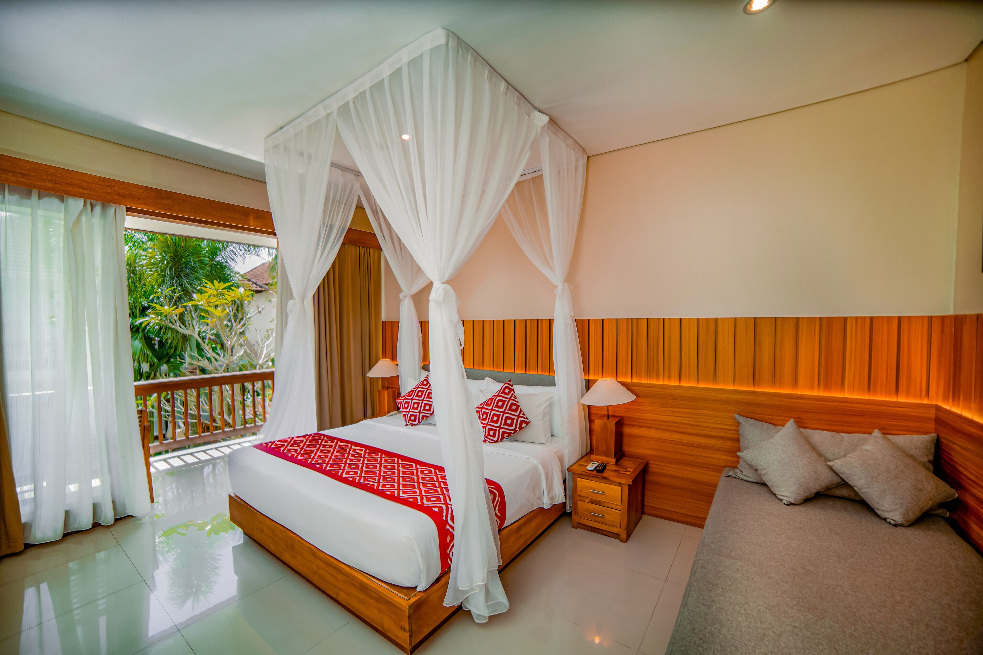 A bedroom with a four-poster canopy bed, a wooden headboard, and a balcony with a view of greenery.