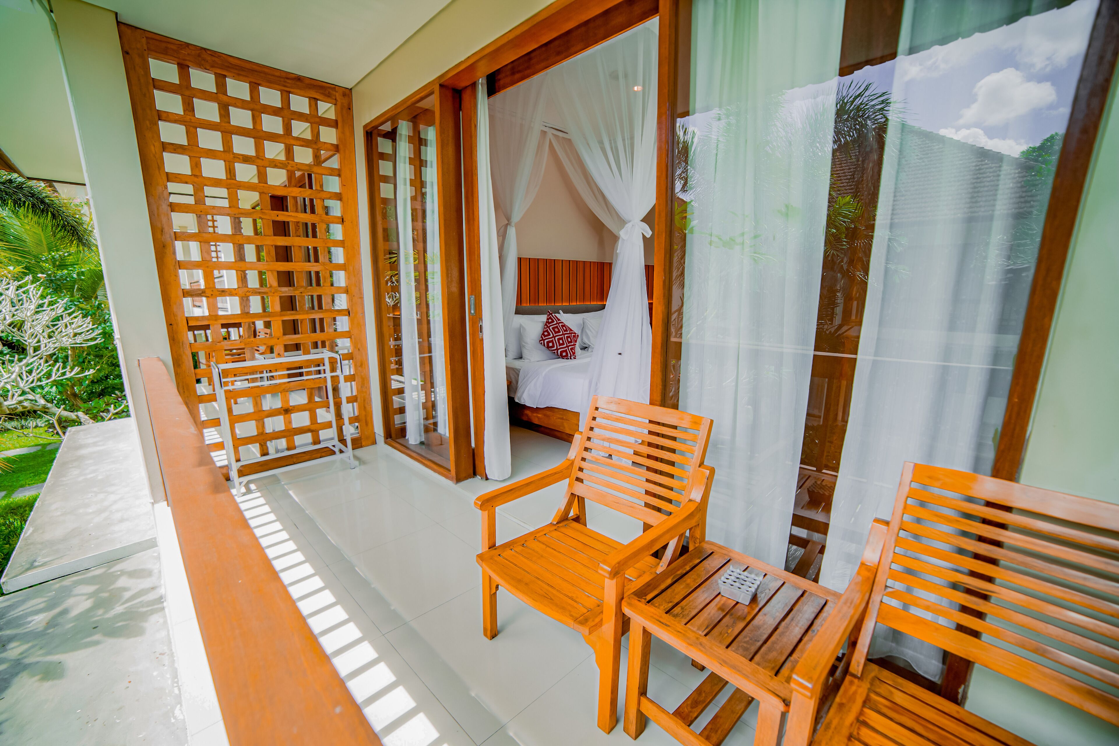 A balcony with wooden chairs and a table, a bed with a canopy, and a view of greenery.