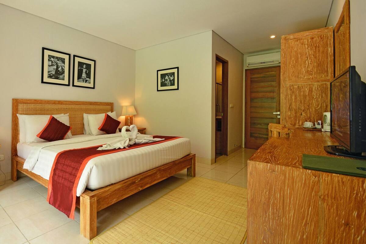 A hotel room with a wooden bed, a bedside table with a lamp, a mirror, and a television.