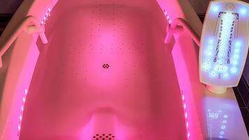 Ett modernt badrum med ett badkar som är upplyst med rosa ljus, en digital kontrollpanel och ett duschmunstycke som kan hållas i handen.