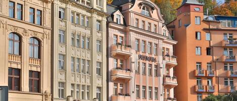 Un edificio a più piani con un ristorante al piano terra, caratterizzato da dettagli architettonici elaborati e balconi con fioriere.