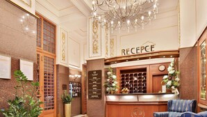 A reception area with a wooden desk, a chandelier, and a red carpet. - Olympia Wellness Hotel (Karlovy Vary)