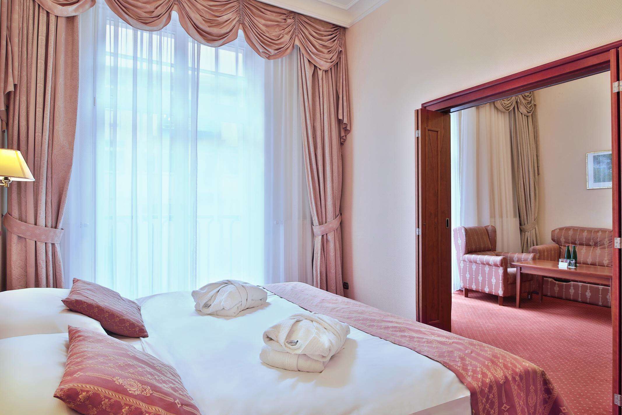 A hotel room with a large bed, two pillows, a robe, a desk, and a chair.