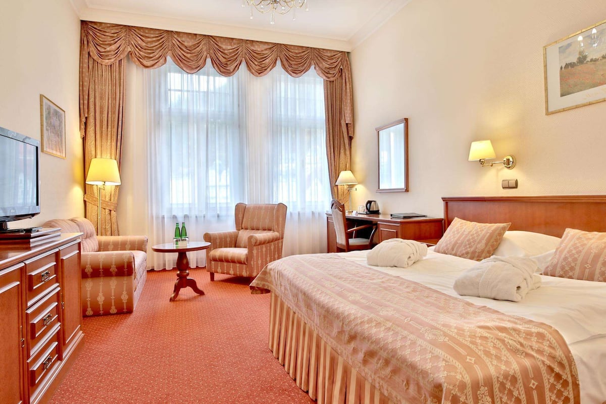 A hotel room with a large bed, a desk, a chair, a television, and a view of the outdoors through the window.