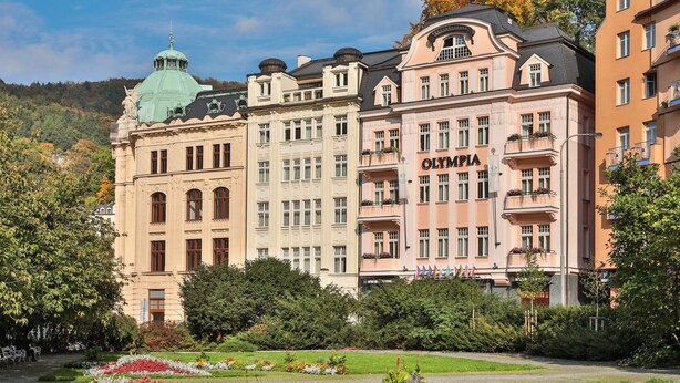 A historic building with the name "OLYMPIA" on the facade, surrounded by lush gardens and a clear sky. - Olympia Wellness Hotel (Karlovy Vary)