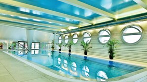 A swimming pool with multiple windows, potted plants, and a tiled floor. - Olympia Wellness Hotel (Karlovy Vary)