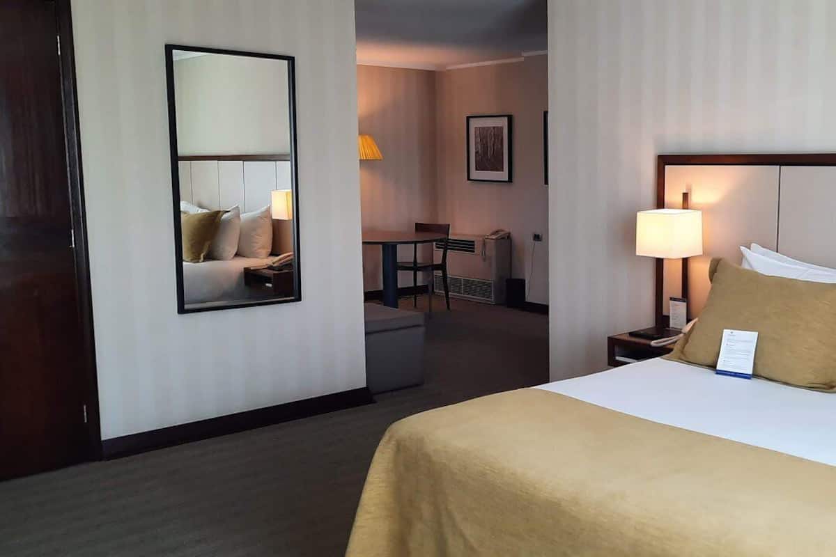 Een hotelkamer met een groot bed, een nachtkastje met lamp, een stoel en een bureau.
