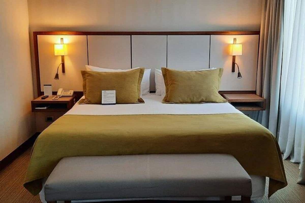 Een hotelkamer met een bed, twee nachtkastjes, een lamp en een raam met gordijnen.