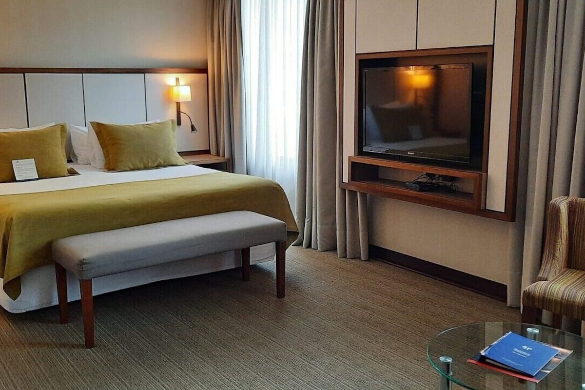 Een hotelkamer met een bed, nachtkastjes, een televisie, een stoel en een glazen salontafel.