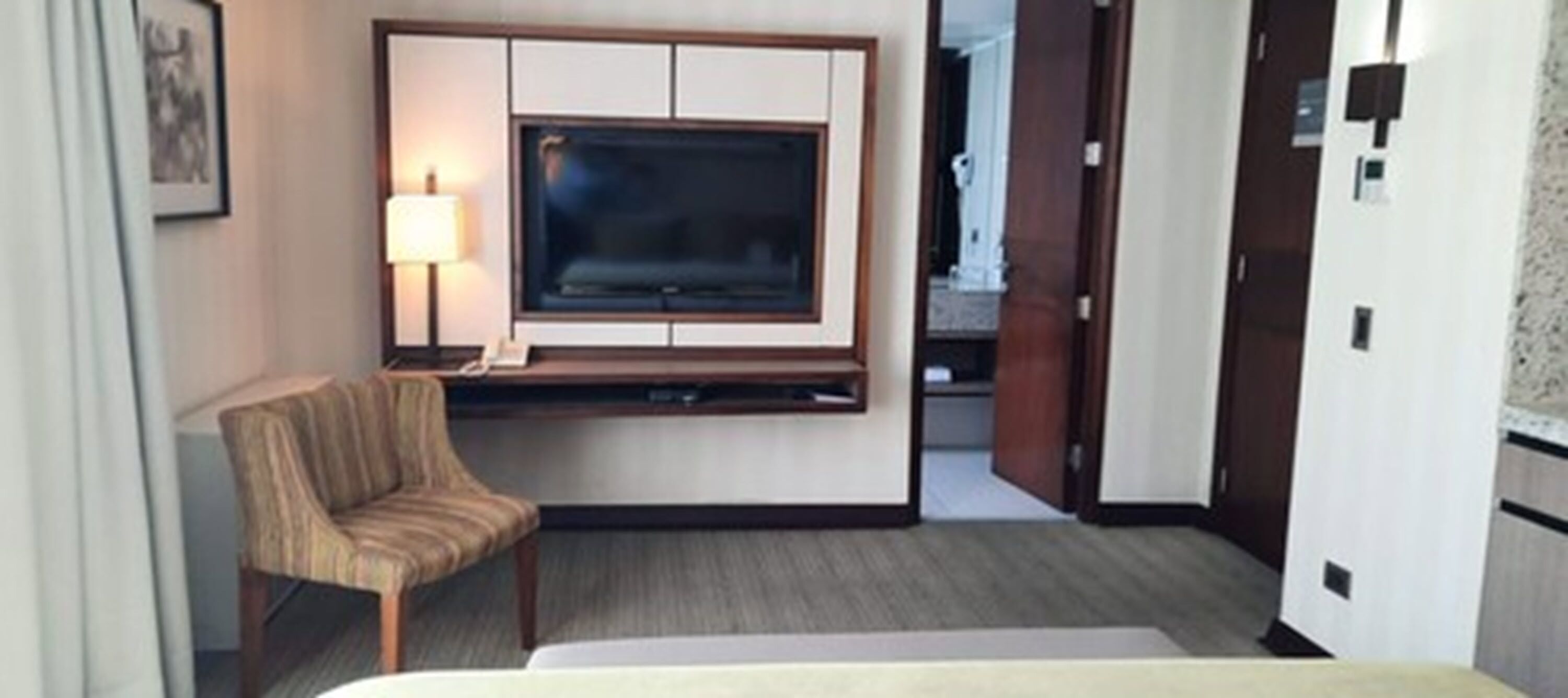 Habitación de hotel con cama, televisor montado en la pared, escritorio con lámpara y una silla.