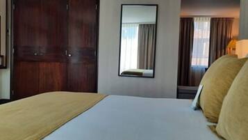 A hotel room with a bed, a TV, a mirror, and a window with curtains.