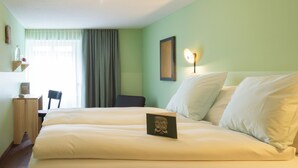 Une chambre d’hôtel avec un grand lit, un bureau, une chaise, une table de chevet et une fenêtre avec des rideaux.