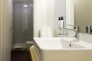 A modern bathroom with a white sink, a glass shower enclosure, and toiletries on the wall.