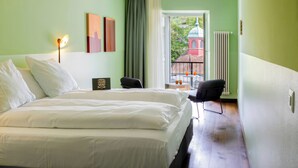 Une chambre d’hôtel avec un grand lit, un bureau avec une chaise, une fenêtre donnant sur un immeuble et un radiateur.