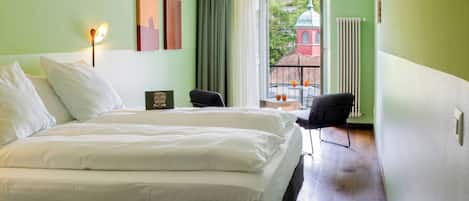 Habitación de hotel con una cama grande, un escritorio con silla, una ventana con vista a un edificio y un radiador.