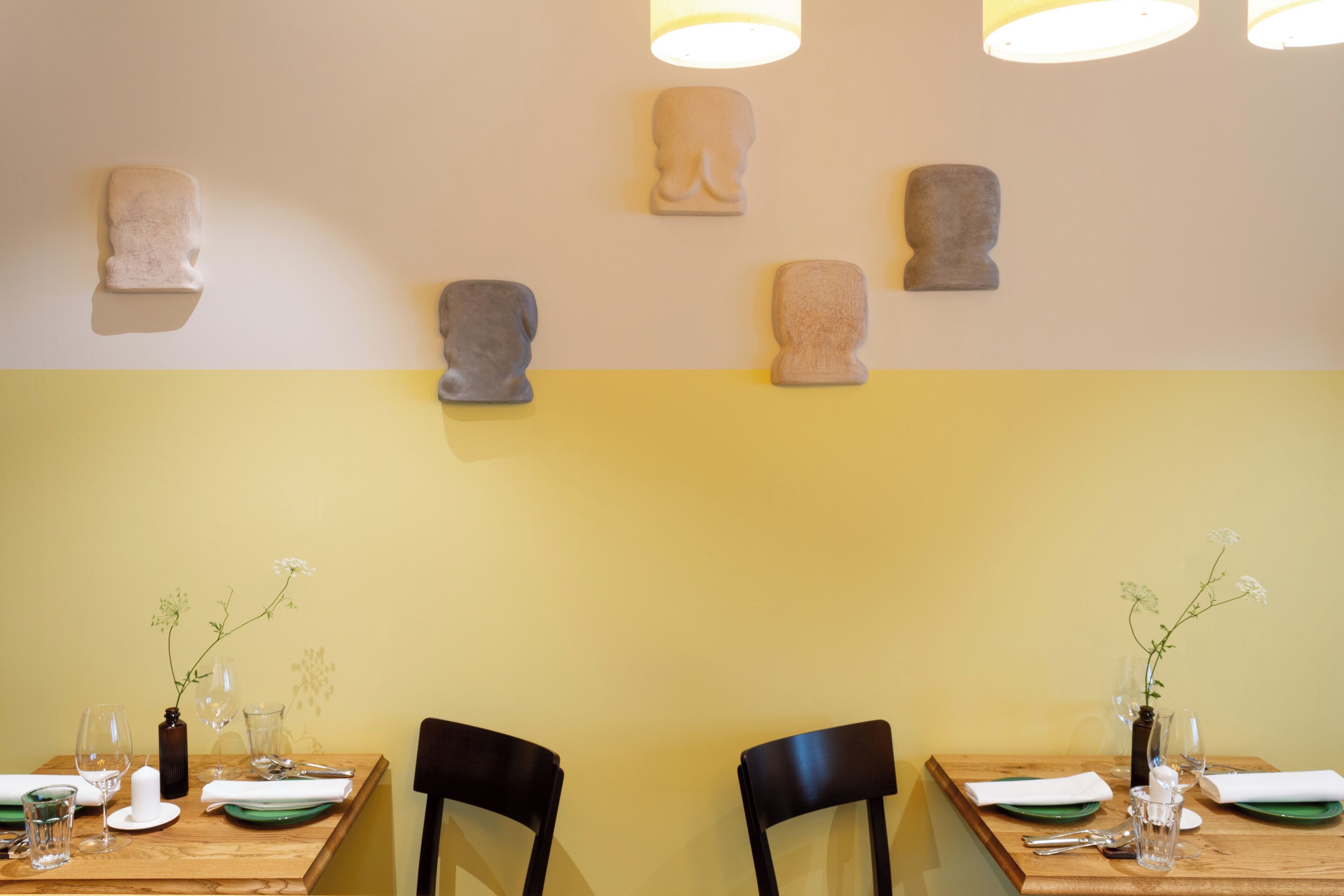 Un comedor con dos mesas, cada una dispuesta con platos, vasos y cubiertos. Encima de las mesas, esculturas fijadas a la pared.