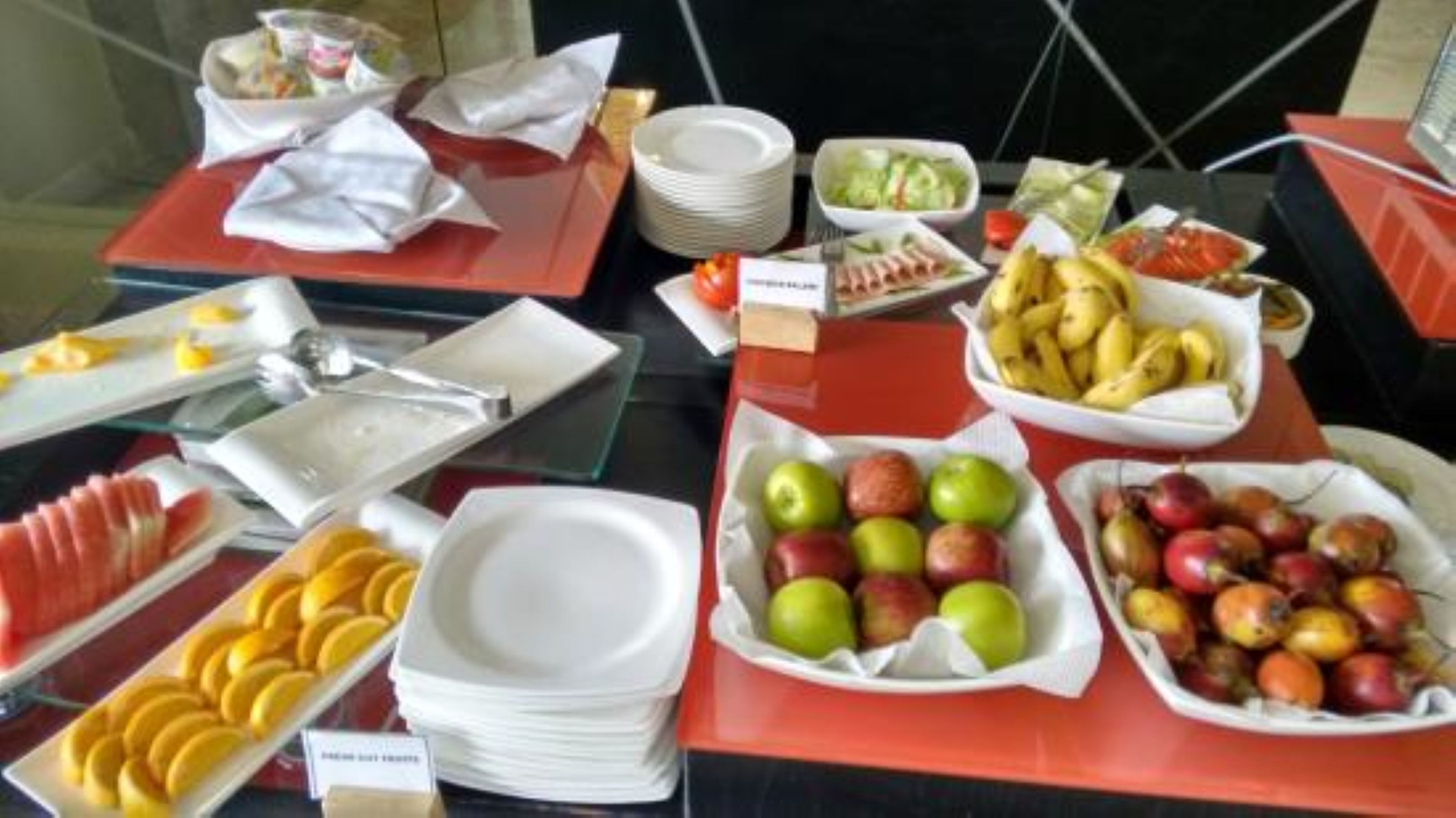A buffet table with various fruits and dishes, including sliced oranges, apples, and bananas.