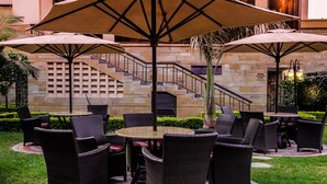 An outdoor patio area with wicker furniture and large umbrellas, a stone staircase, and a sign warning against smoking. - Waridi Paradise Hotel & Suites (Nairobi)