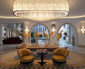 A lobby with a grand chandelier, two leather armchairs, a central table with floral arrangements, and a reception desk. - Waldorf Astoria Jerusalem (Jerusalem)